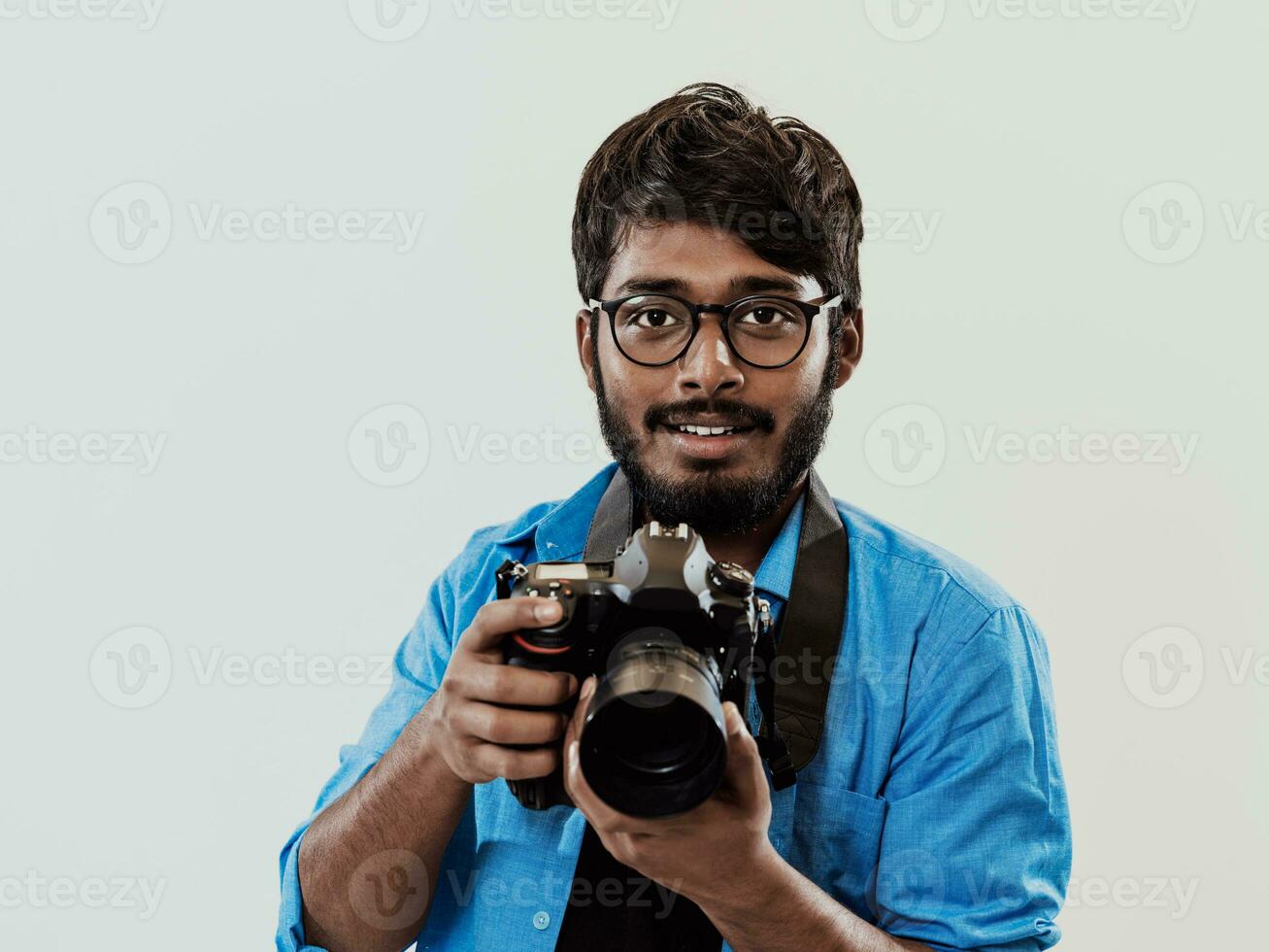 profesional fotógrafo teniendo dslr cámara tomando imagen.indio hombre fotografía entusiasta tomando foto mientras en pie en azul antecedentes. estudio Disparo