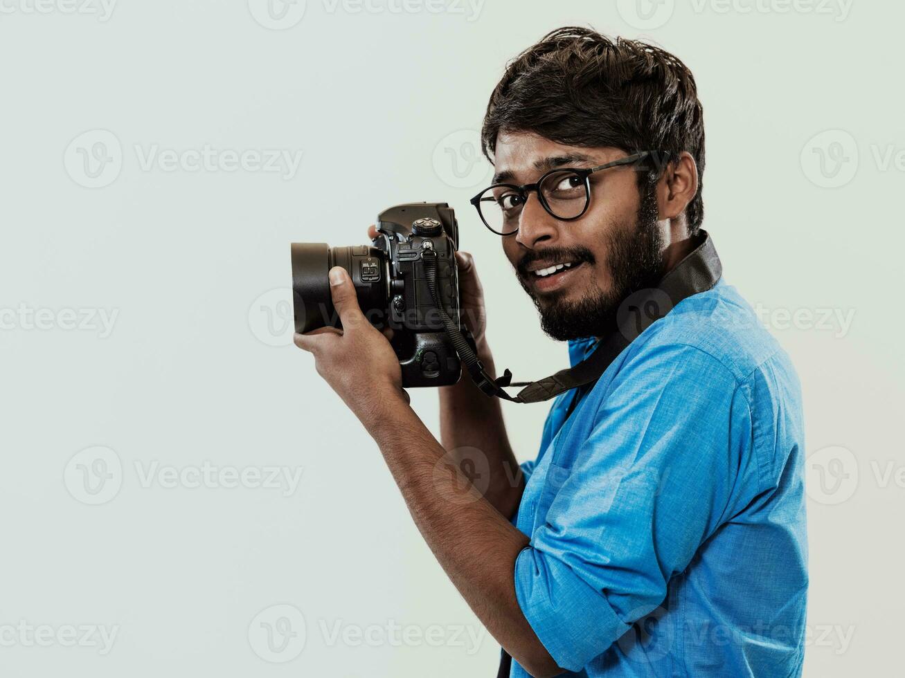 Professional photographer having DSLR camera taking picture.Indian man photography enthusiast taking photo while standing on blue background. Studio shot