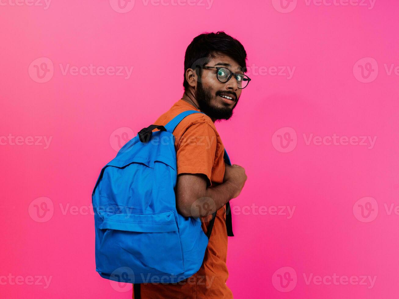 Indian student with blue backpack, glasses and notebook posing on pink background. The concept of education and schooling. Time to go back to school photo