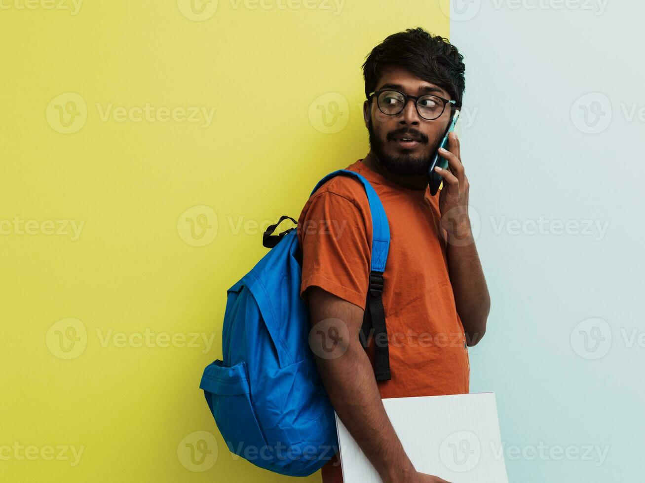 indio estudiante con azul mochila, lentes y cuaderno posando en gris y verde antecedentes. el concepto de educación y enseñanza. hora a Vamos espalda a colegio foto