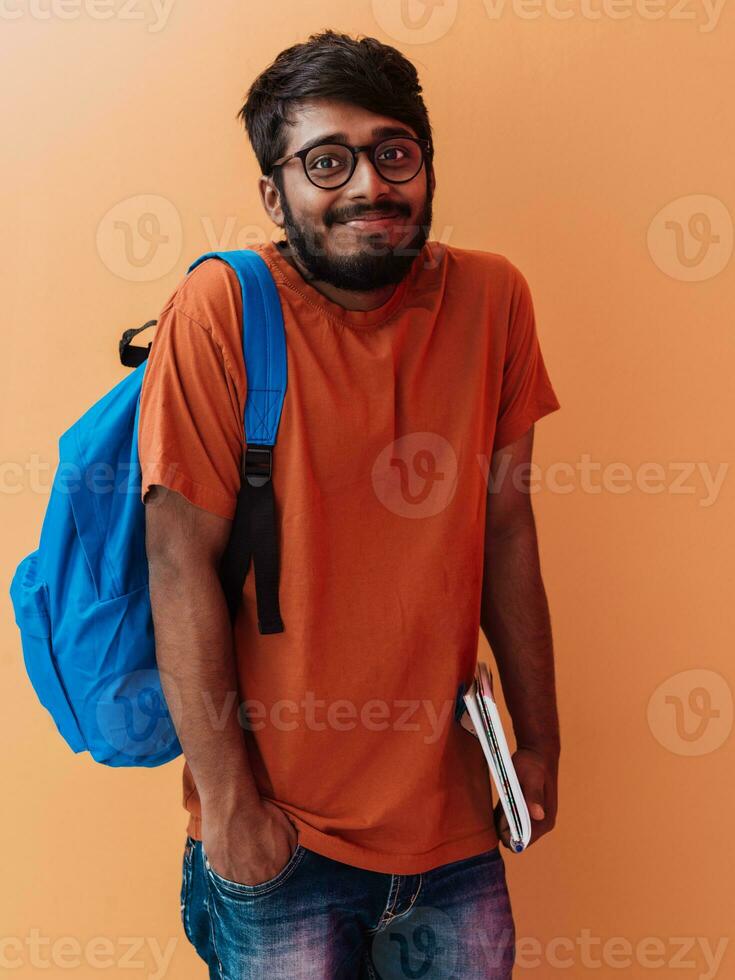 Indian student with blue backpack, glasses and notebook posing on orange background. The concept of education and schooling. Time to go back to school photo