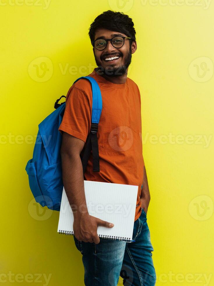 Indian student with blue backpack, glasses and notebook posing on green background. The concept of education and schooling. Time to go back to school photo