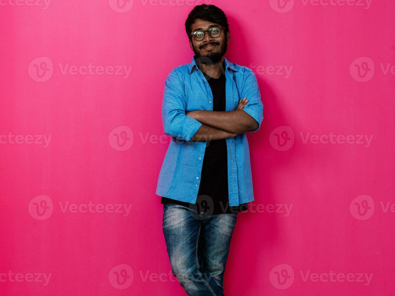 Indian smiling young student in blue shirt and glasses posing on pink background photo