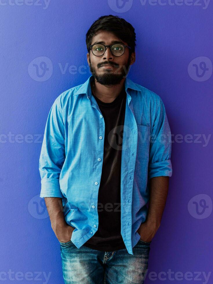 indio sonriente joven hombre con azul camisa y lentes posando en púrpura antecedentes foto