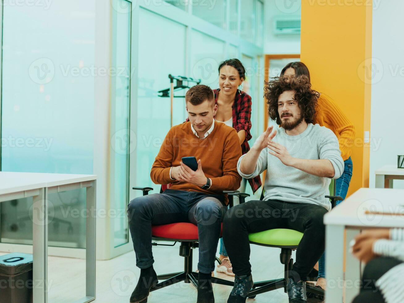 Team building and office fun. Young cheerful businesspeople in smart casual wear having fun while racing on office chairs and smiling. photo