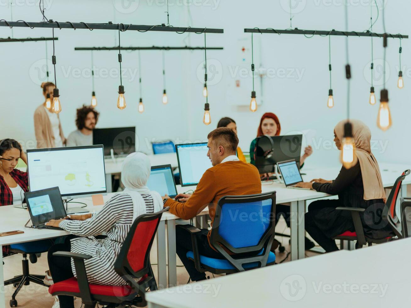 Group of multi-ethnic colleagues working on desktop computers, laptop and sharing their ideas in a modern office space.Young influencers work on online marketing projects. photo