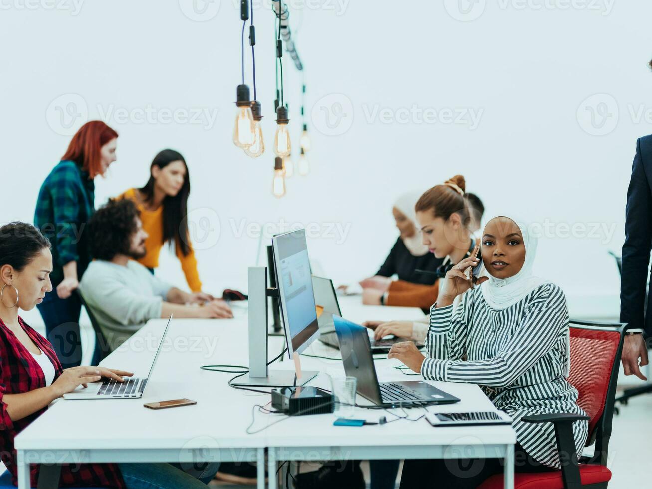 grupo de multiétnico colegas trabajando en escritorio ordenadores, ordenador portátil y compartiendo su ideas en un moderno oficina espacio.joven influencers trabajo en en línea márketing proyectos foto