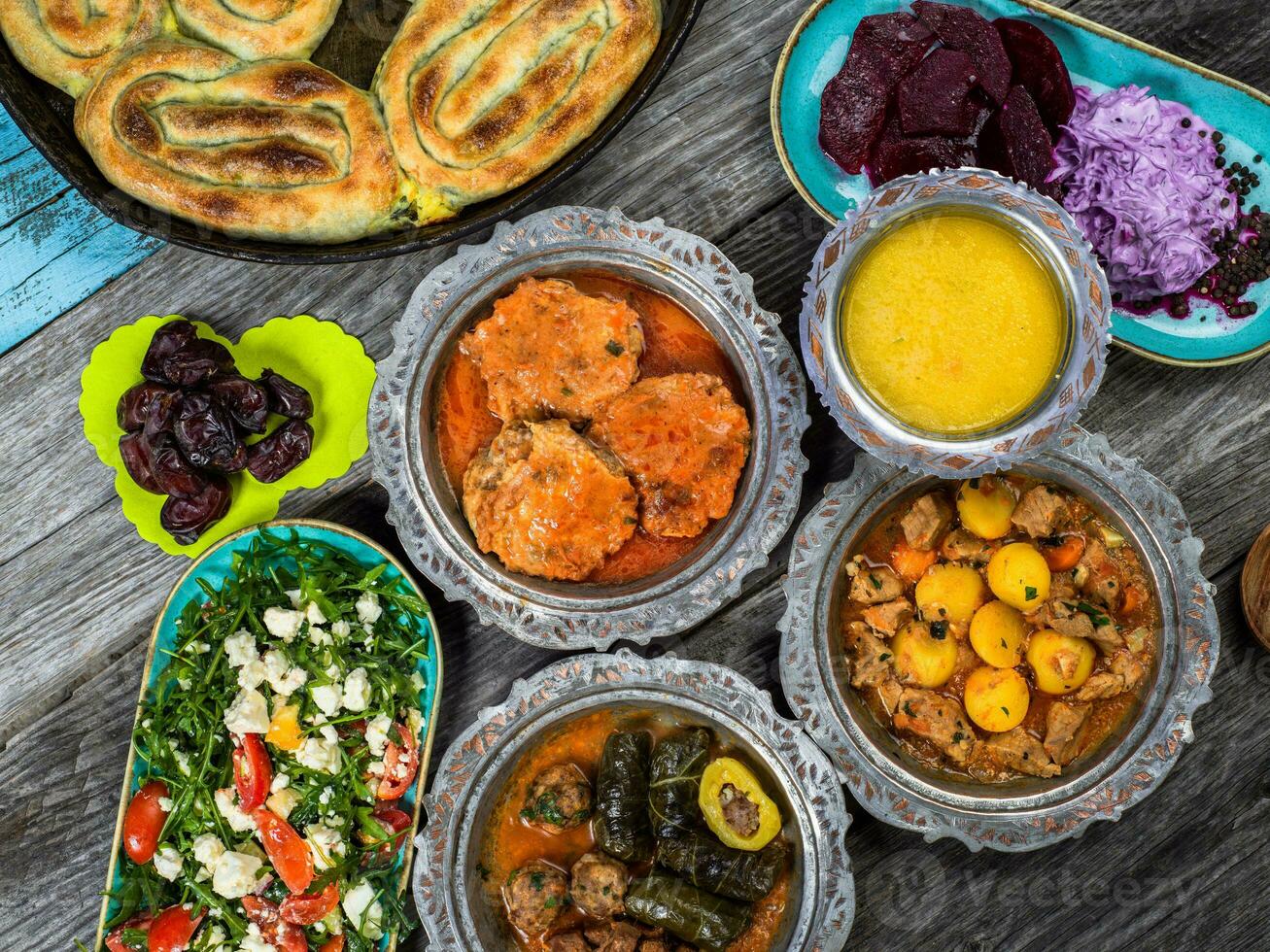 Eid Mubarak Traditional Ramadan Iftar dinner. Assorted tasty food in authentic rustic dishes on wooden blue background. Turkish Bosnian food meat kebab, pita, Sarma, klepe, sogan dolma. photo