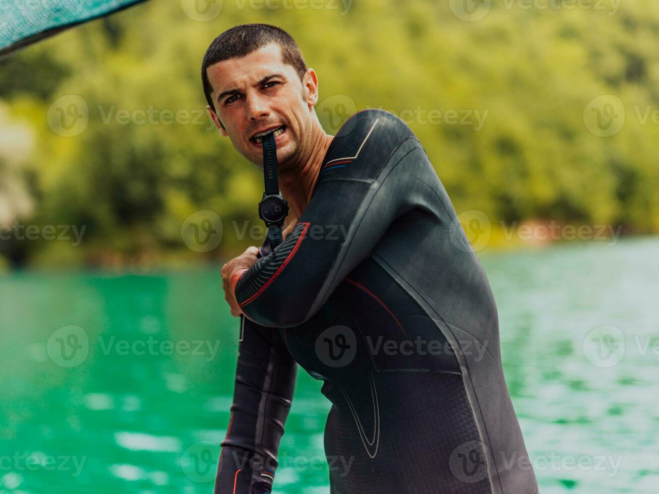 Athlete putting on a swimming suit and preparing for triathlon swimming and training in the river surrounded by natural greenery photo