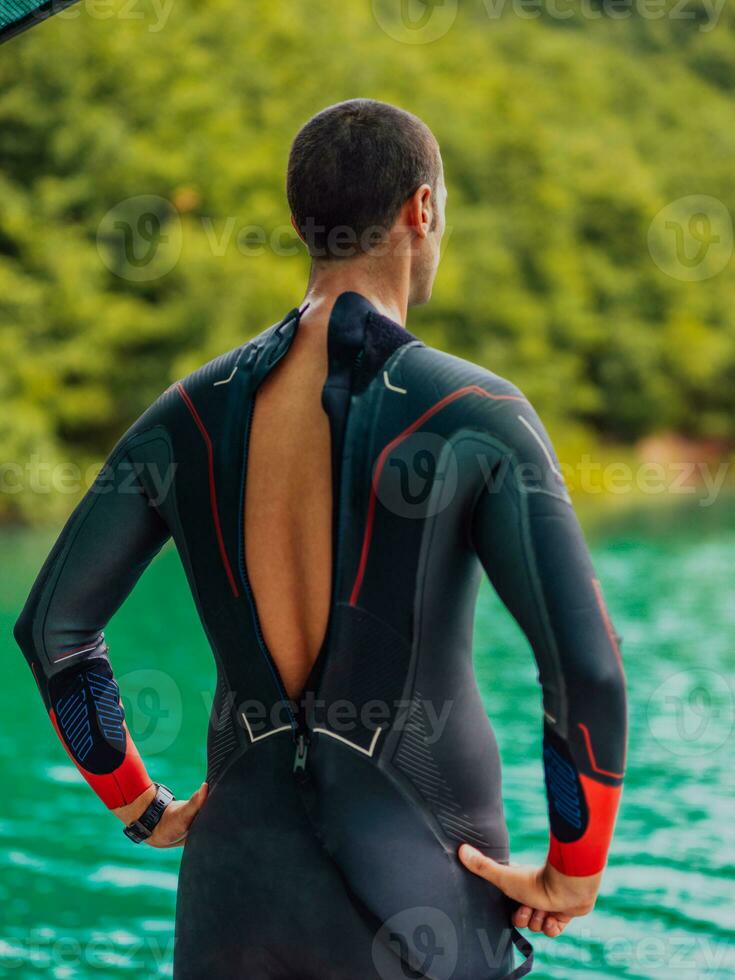 Athlete putting on a swimming suit and preparing for triathlon swimming and training in the river surrounded by natural greenery photo