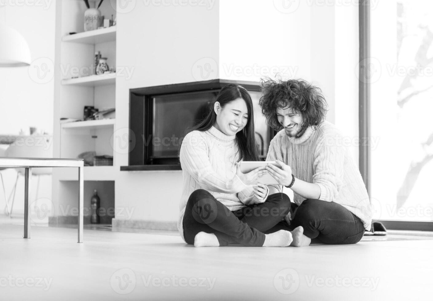 multiethnic couple using tablet computer in front of fireplace photo