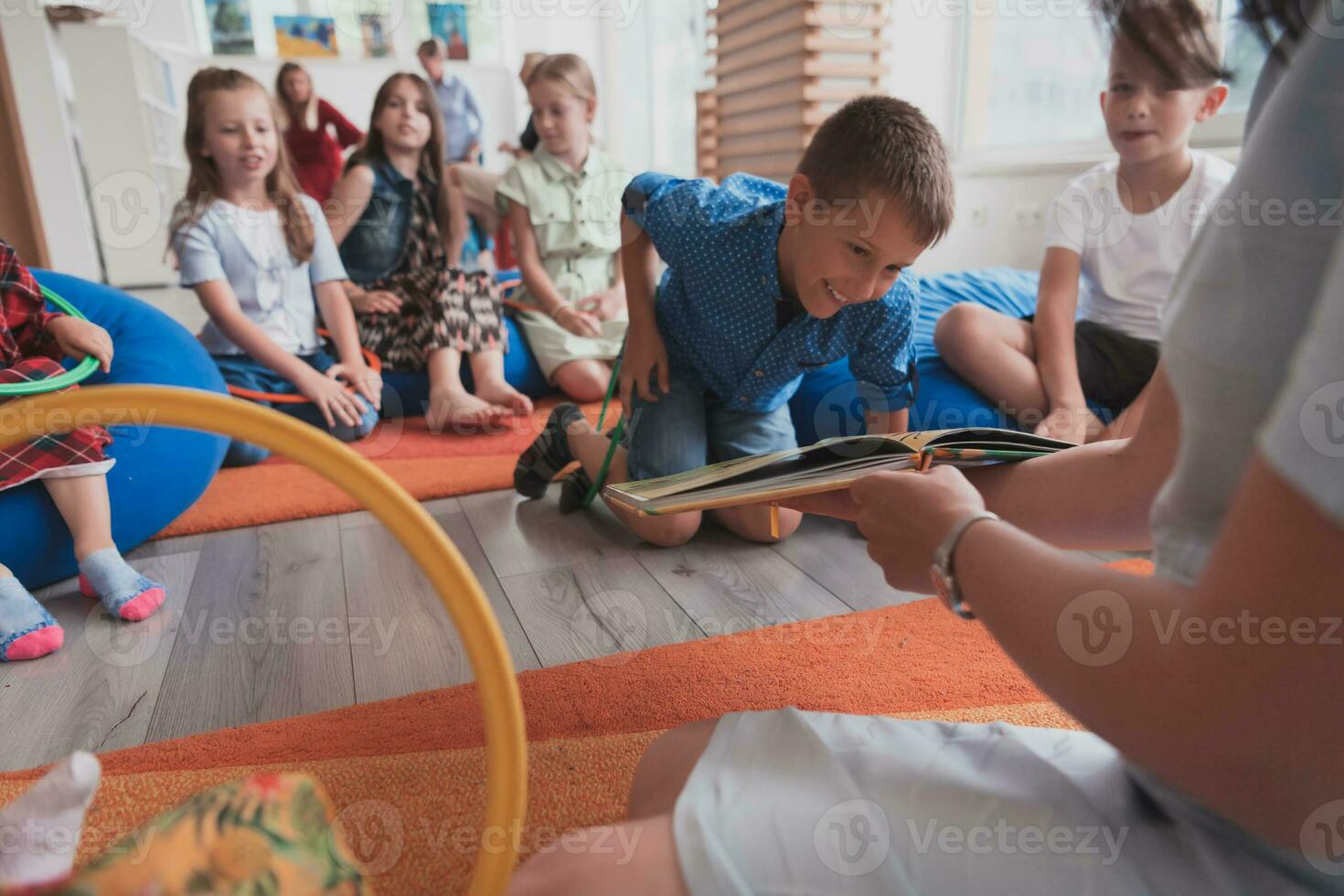 A happy female teacher sitting and playing hand games with a group of little schoolchildren photo