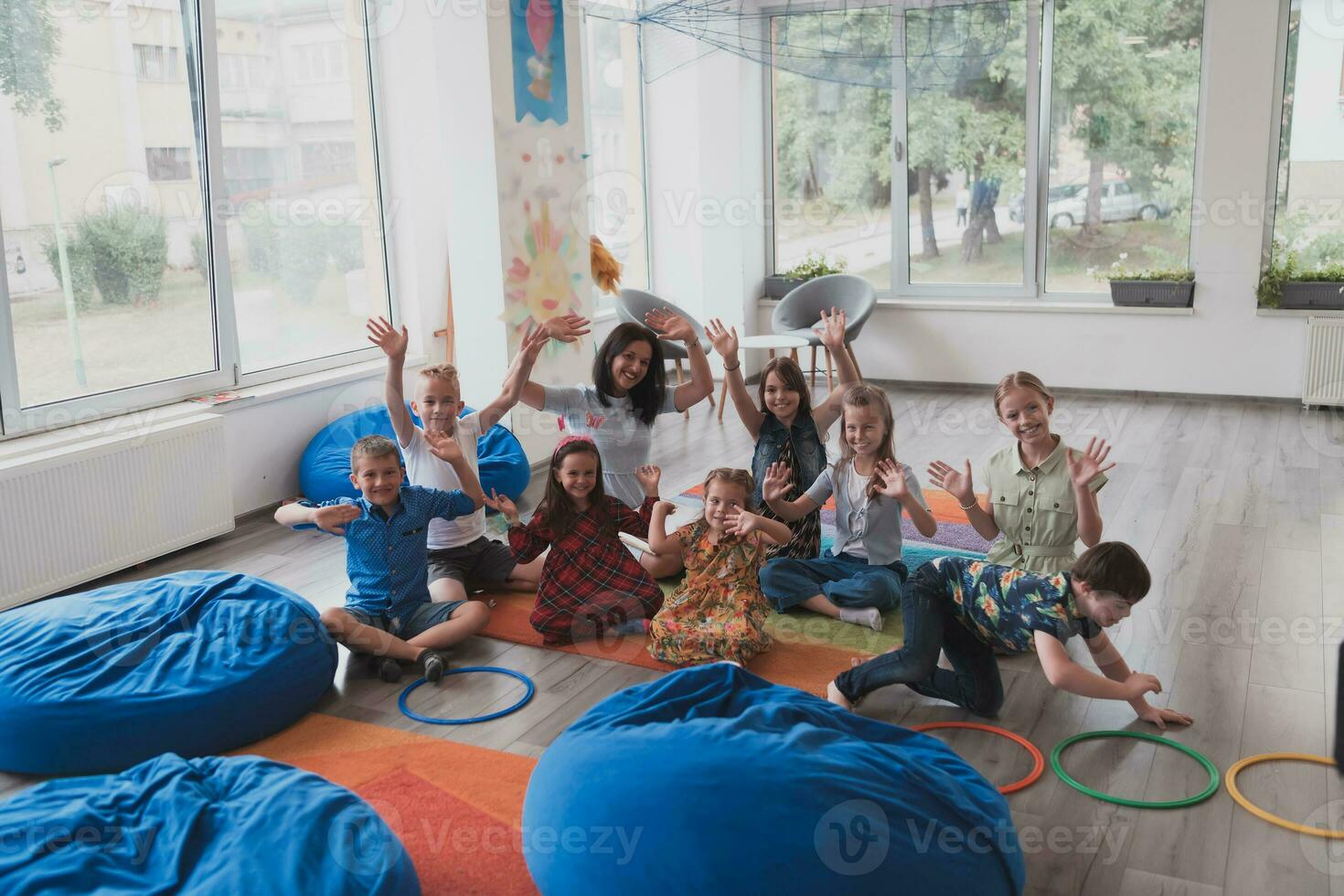 un contento hembra profesor sentado y jugando mano juegos con un grupo de pequeño Niños de escuela foto