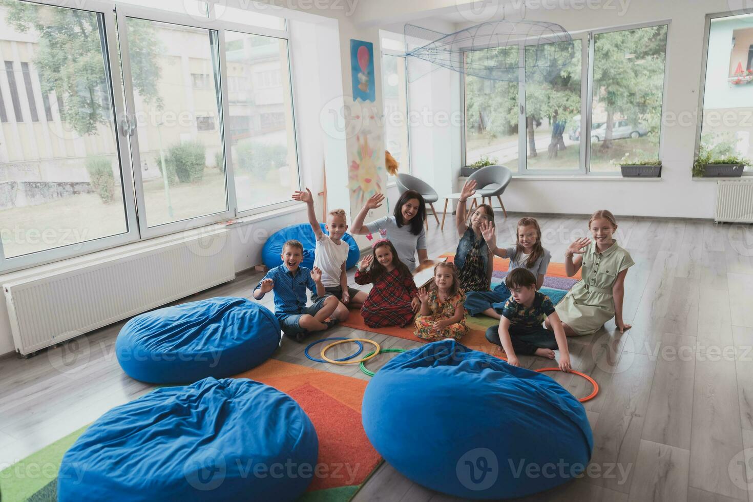 un contento hembra profesor sentado y jugando mano juegos con un grupo de pequeño Niños de escuela foto