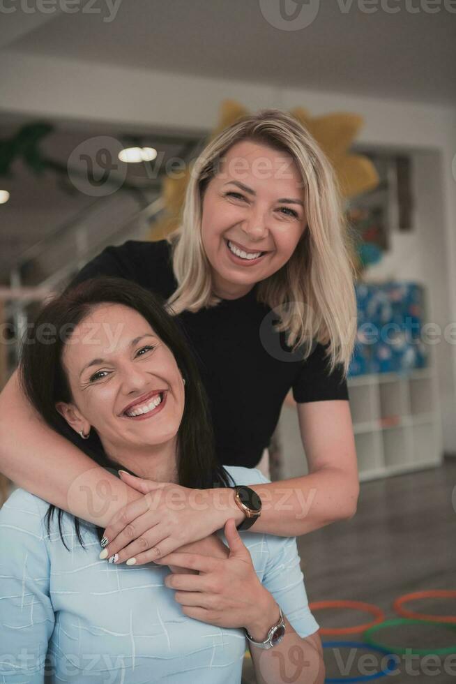 Portrait of two hugging female teachers in a preschool institution, in the background of the classrooms photo