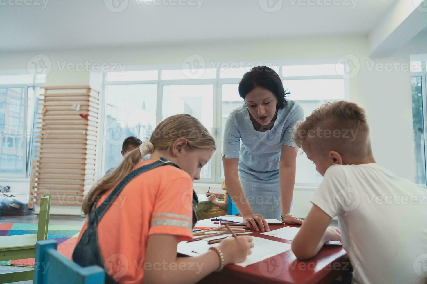 Creative kids during an art class in a daycare center or elementary school classroom drawing with female teacher. photo