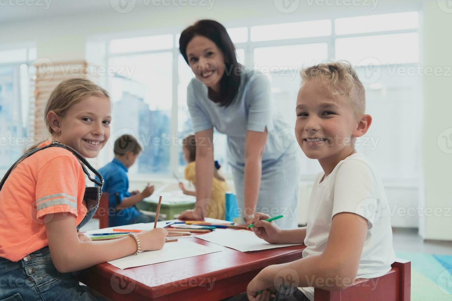 Creative kids during an art class in a daycare center or elementary school classroom drawing with female teacher. photo