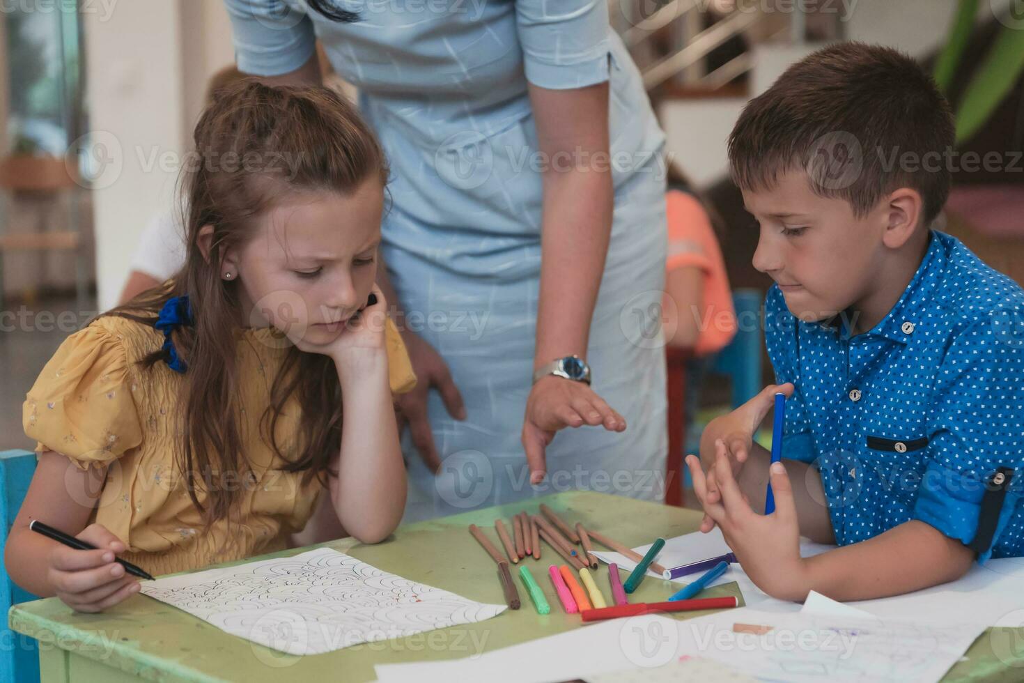 Creative kids during an art class in a daycare center or elementary school classroom drawing with female teacher. photo