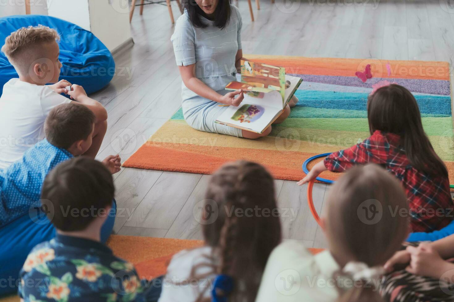 A happy female teacher sitting and playing hand games with a group of little schoolchildren photo