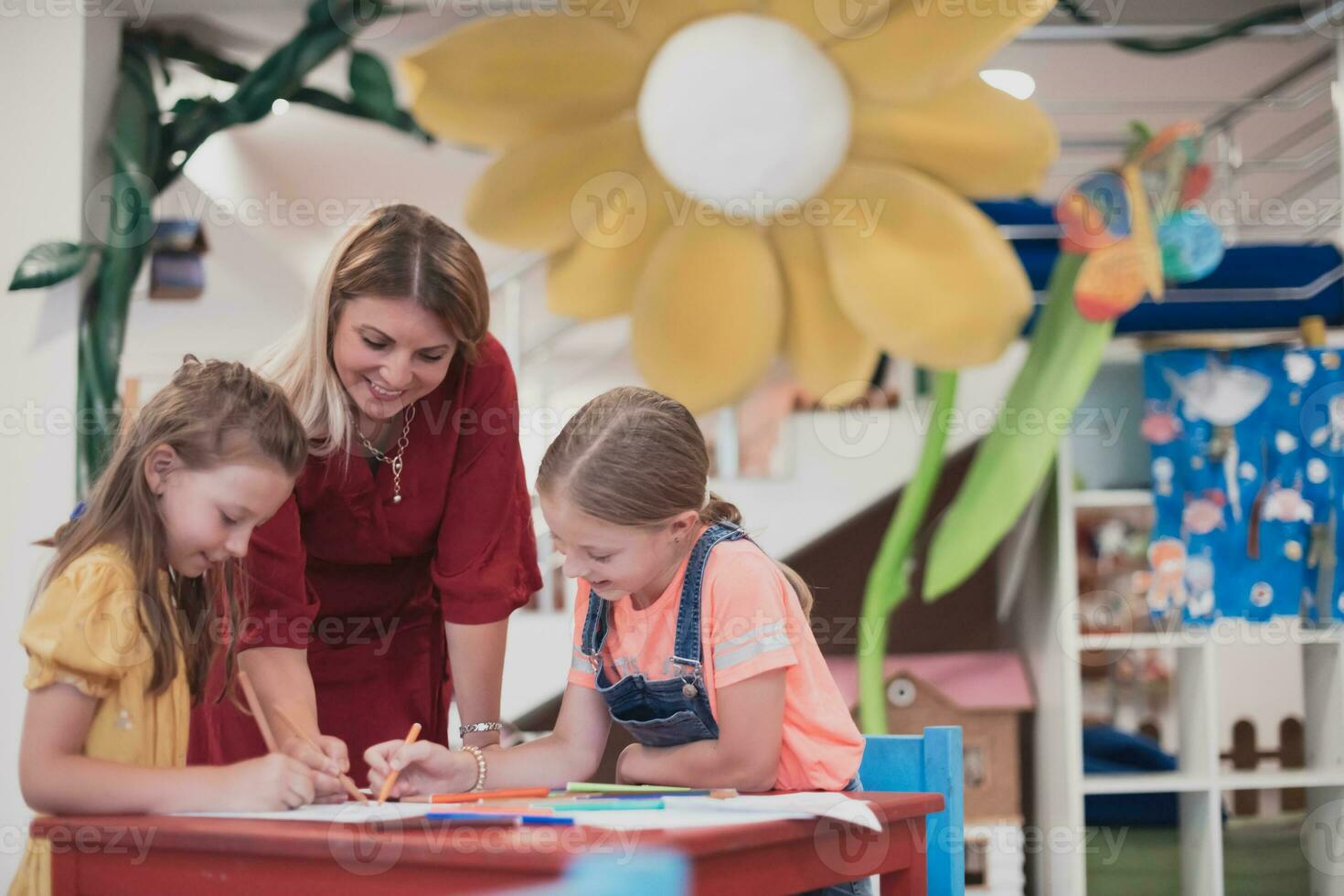 Creative kids during an art class in a daycare center or elementary school classroom drawing with female teacher. photo