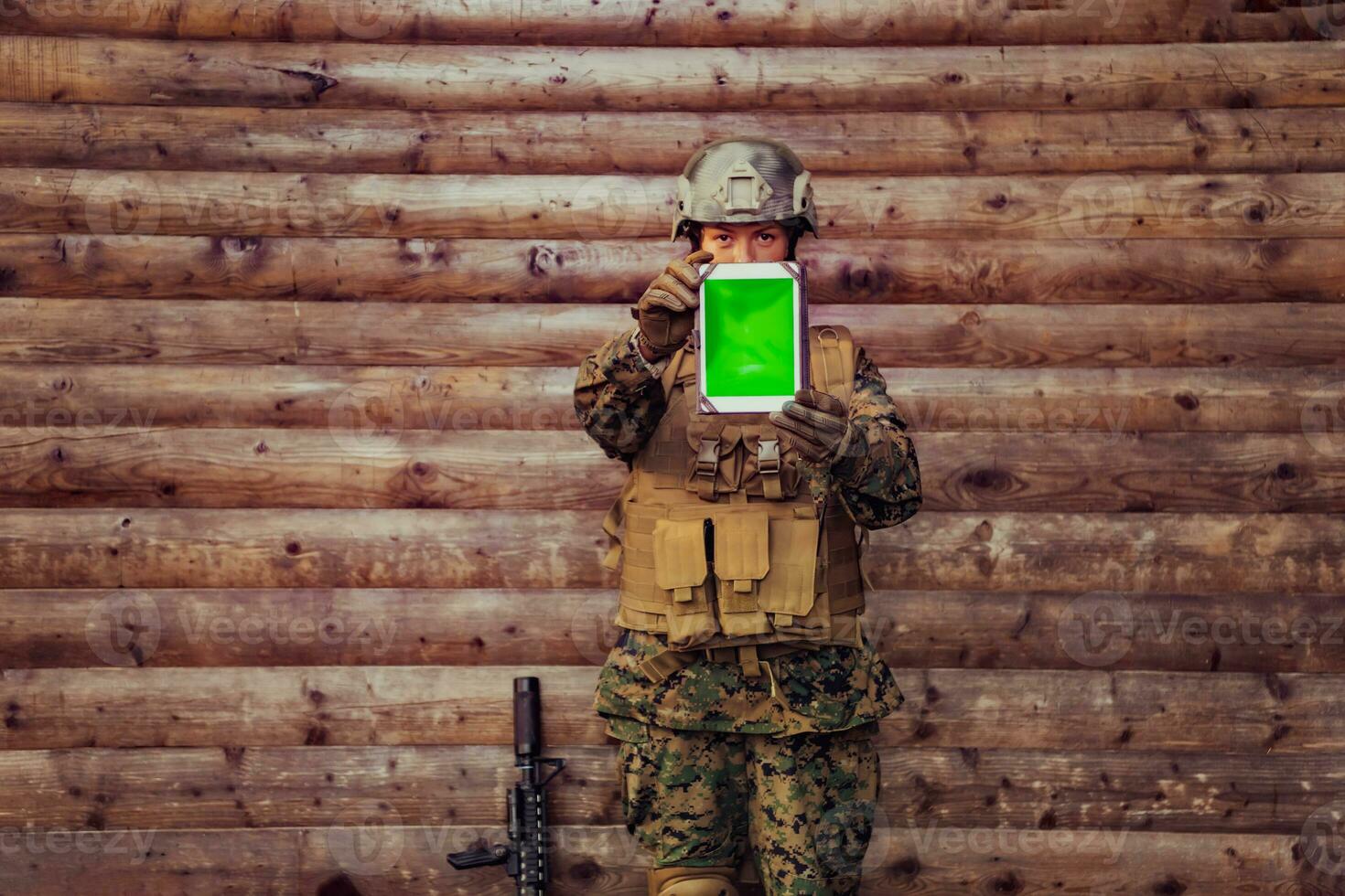 Woman soldier using tablet computer against old wooden wall in camp photo