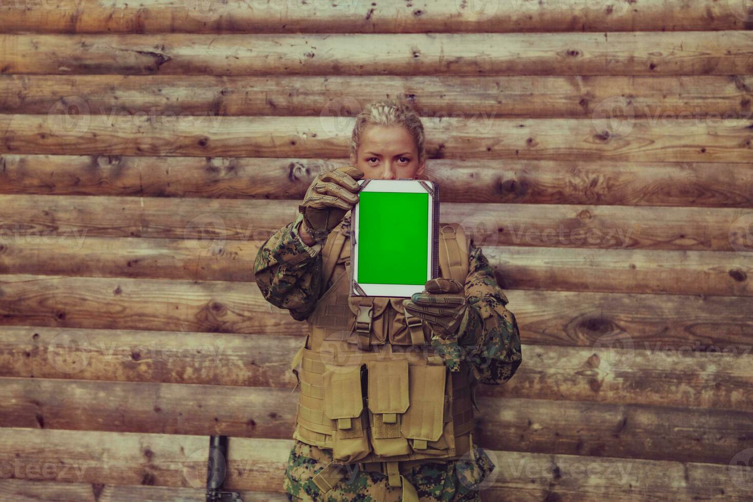 Woman soldier using tablet computer against old wooden wall in camp photo