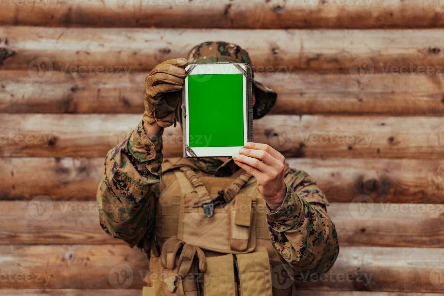 Soldier using tablet computer against old wooden wall in military camp to stay in contact with friends and family photo