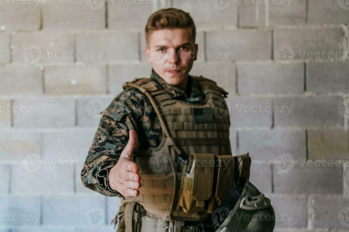 A soldier in uniform stands in front of a stone wall with an outstretched hand. The concept of military and war partnership photo