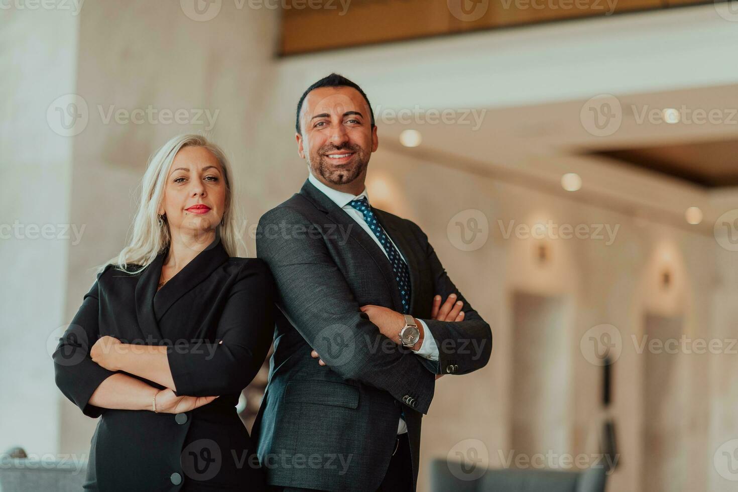 Portrait photo of businessman and businesswoman with crossed arms standing in modern corporation. Selective focus