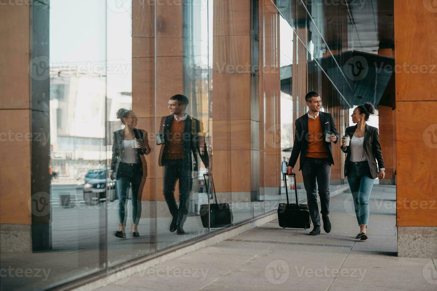 Business man and business woman talking and holding luggage traveling on a business trip, carrying fresh coffee in their hands.Business concept photo