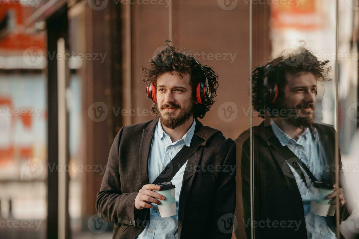 Trendy businessman with leather briefcase in financial district using smartphone while listening audio songs headphones drinking coffee photo