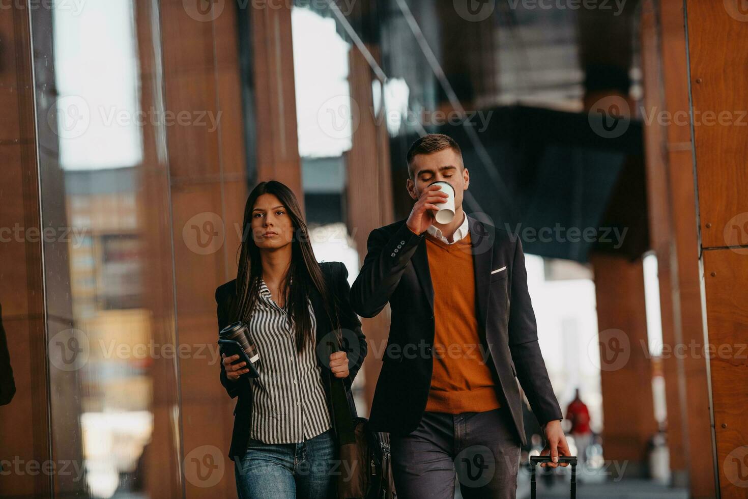 Business man and business woman talking and holding luggage traveling on a business trip, carrying fresh coffee in their hands.Business concept photo