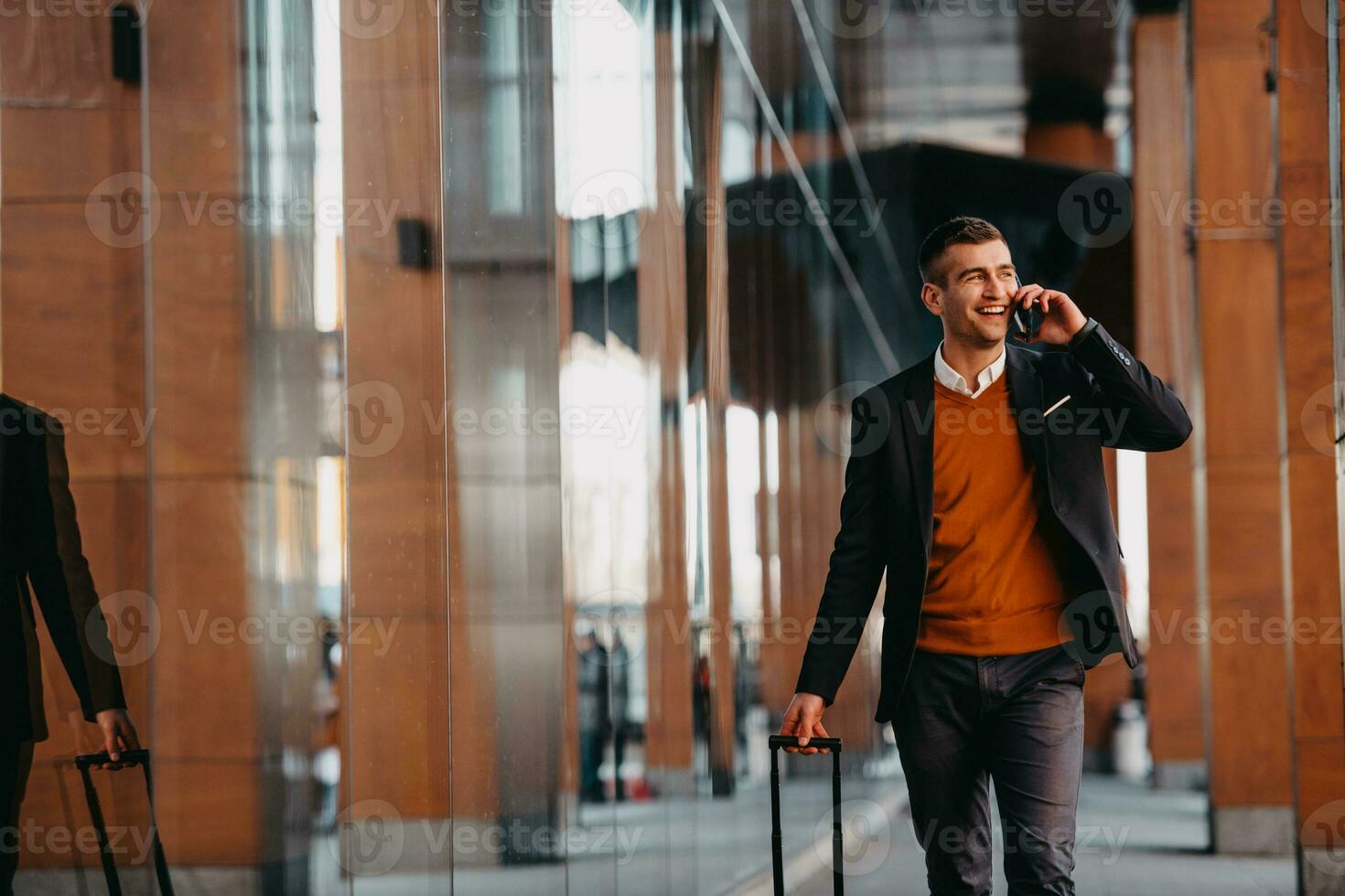 Going to airport terminal. Confident businessman traveler walking on city streets and pulling his suitcase drinking coffee and speaking on smartphone photo