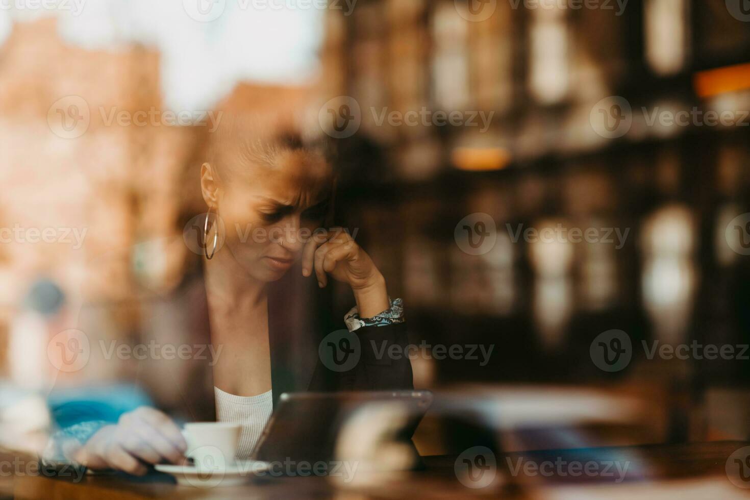 woman in a coffee shop drink coffee viewed through glass with reflections as they sit at a table chatting and laughing photo