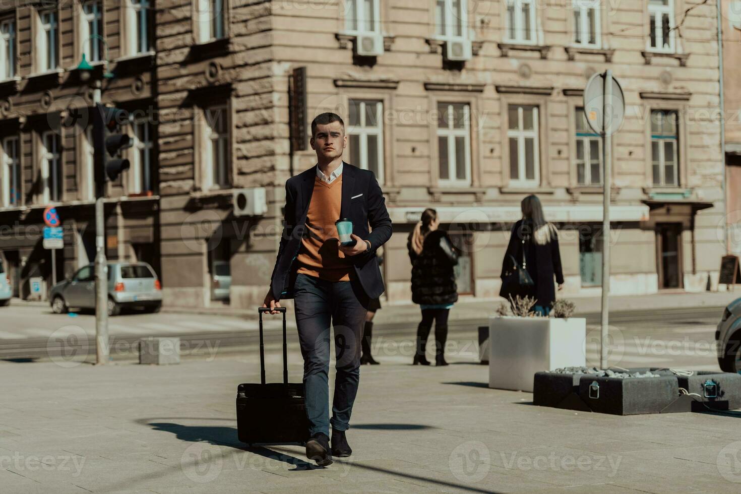 Going to airport terminal. Confident businessman traveler walking on city streets and pulling his suitcase drinking coffee and speaking on smartphone photo