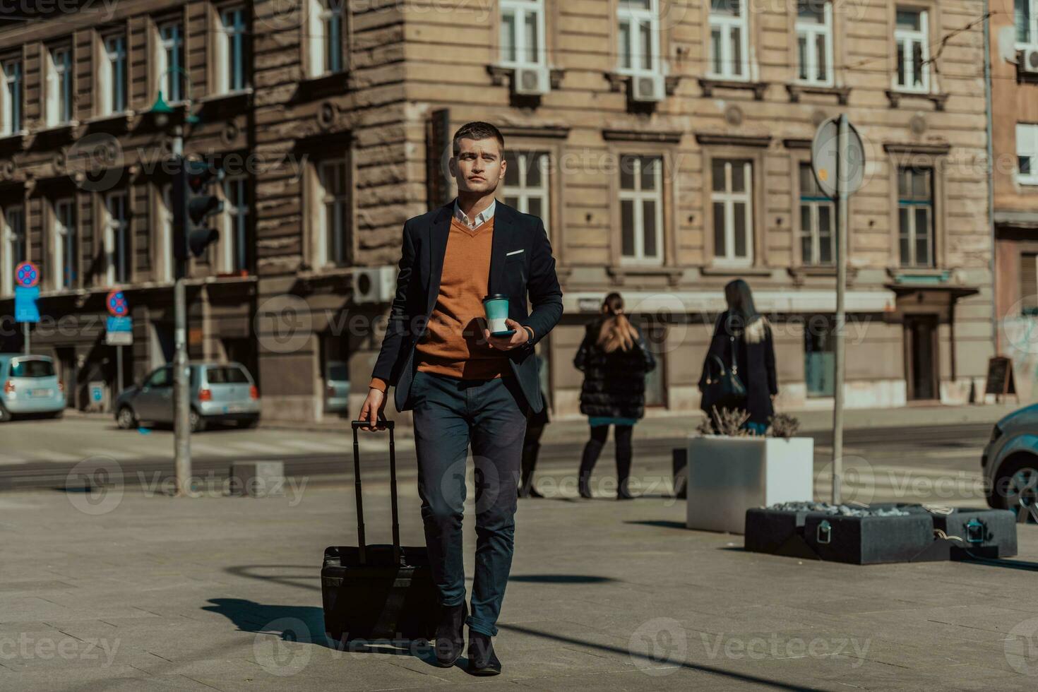 Going to airport terminal. Confident businessman traveler walking on city streets and pulling his suitcase drinking coffee and speaking on smartphone photo