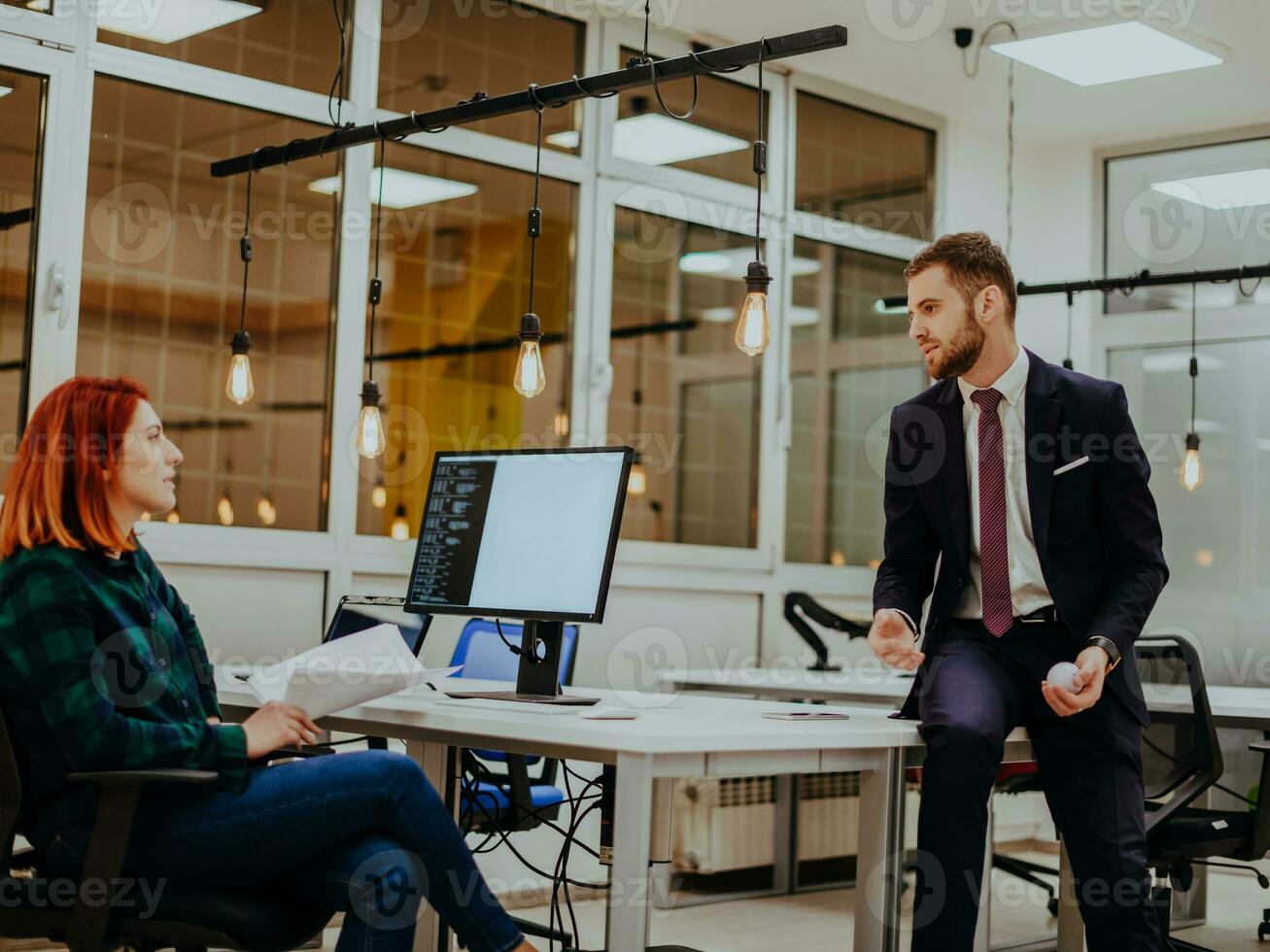 The boss of the company is talking to his colleague who is working on a project in a modern office photo