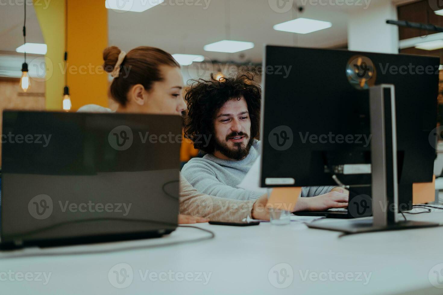 Two colleagues working on a project in modern startup offices. Guy with afro haircut and a female blonde employee working at the office. photo