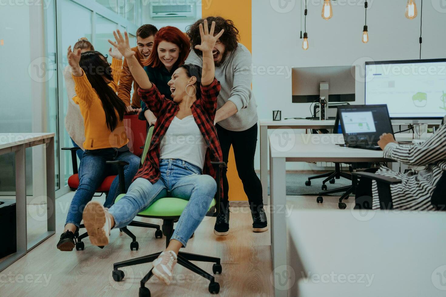 Team building and office fun. Young cheerful businesspeople in smart casual wear having fun while racing on office chairs and smiling. photo