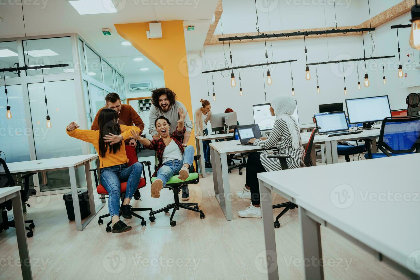 Team building and office fun. Young cheerful businesspeople in smart casual wear having fun while racing on office chairs and smiling. photo