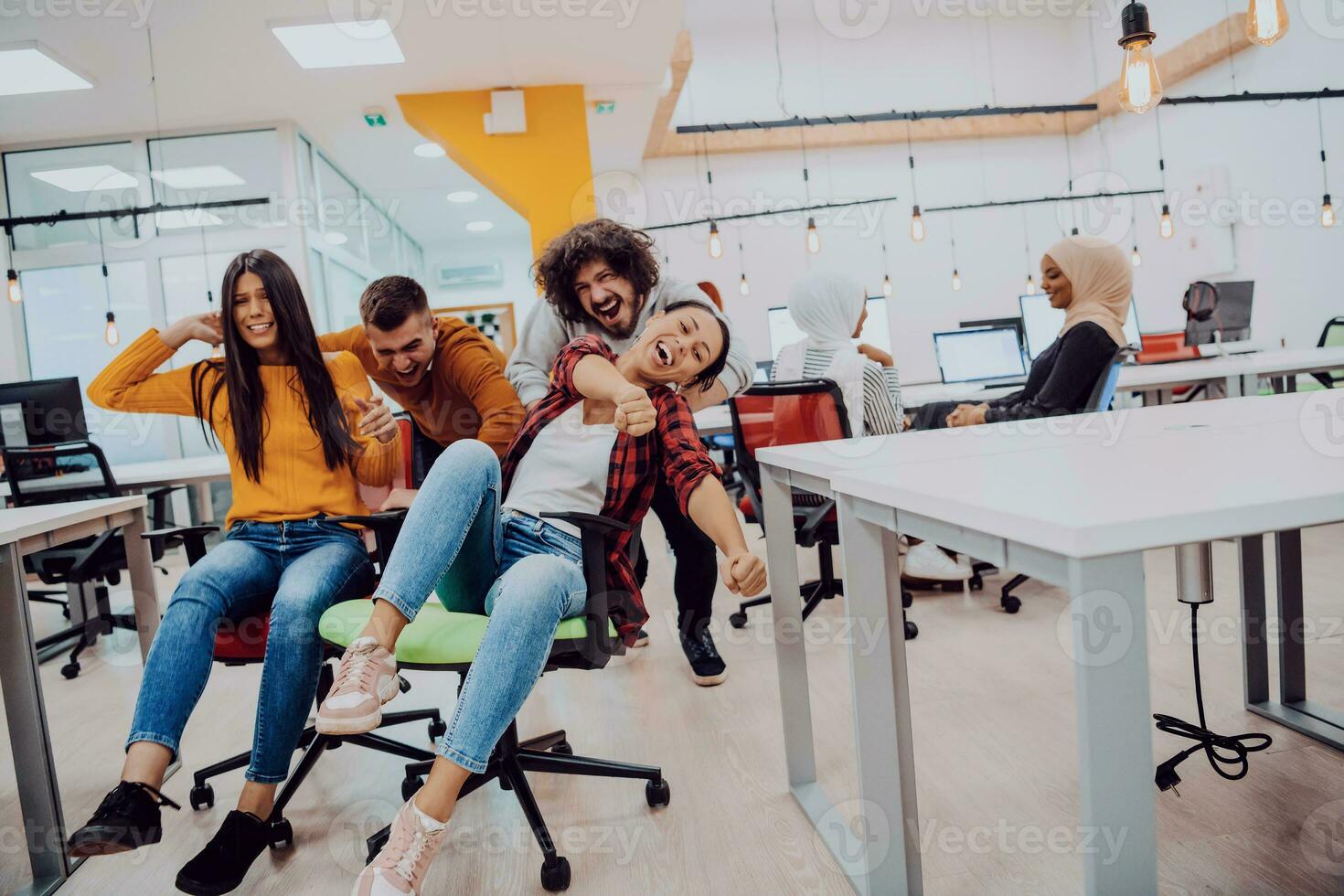 Team building and office fun. Young cheerful businesspeople in smart casual wear having fun while racing on office chairs and smiling. photo