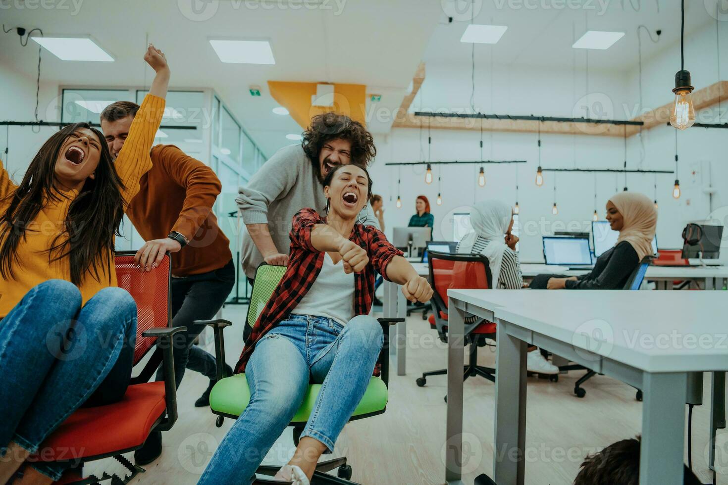 Team building and office fun. Young cheerful businesspeople in smart casual wear having fun while racing on office chairs and smiling. photo