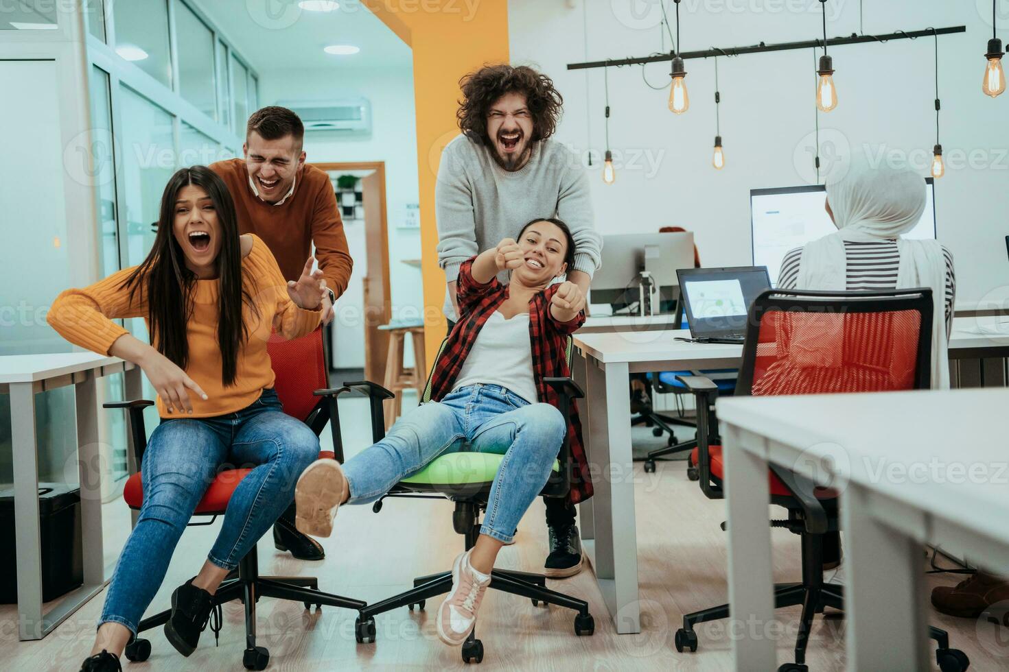 Team building and office fun. Young cheerful businesspeople in smart casual wear having fun while racing on office chairs and smiling. photo