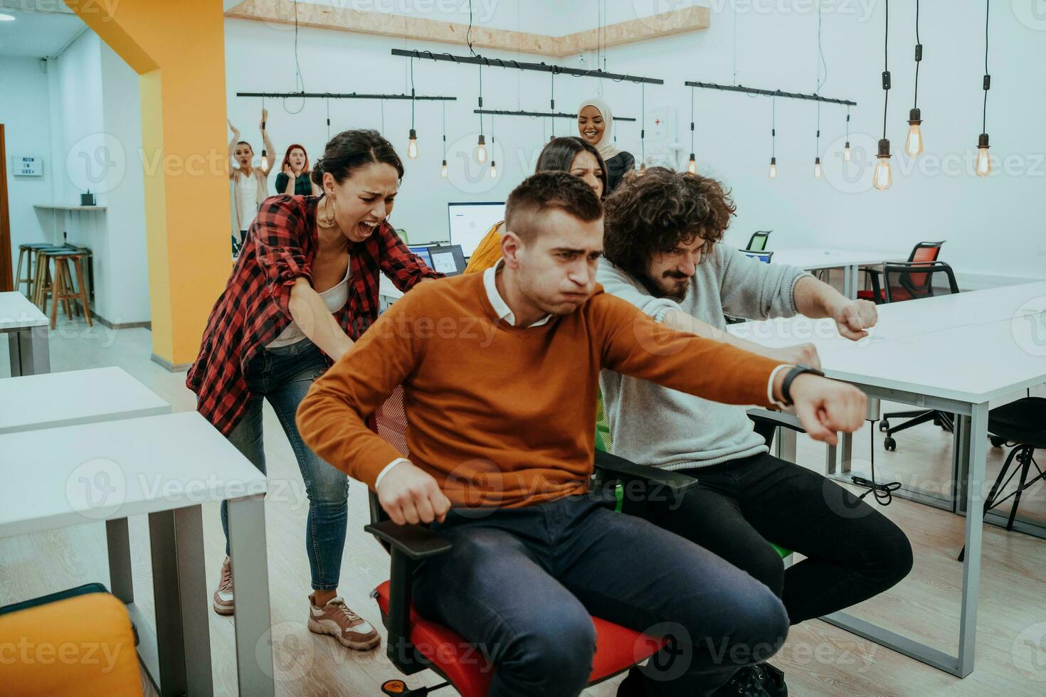 Team building and office fun. Young cheerful businesspeople in smart casual wear having fun while racing on office chairs and smiling. photo