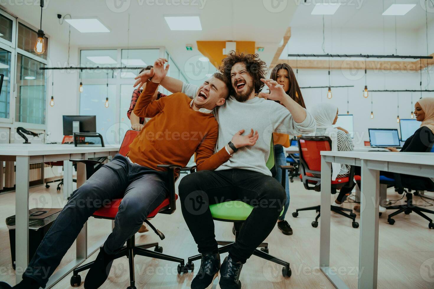 Team building and office fun. Young cheerful businesspeople in smart casual wear having fun while racing on office chairs and smiling. photo