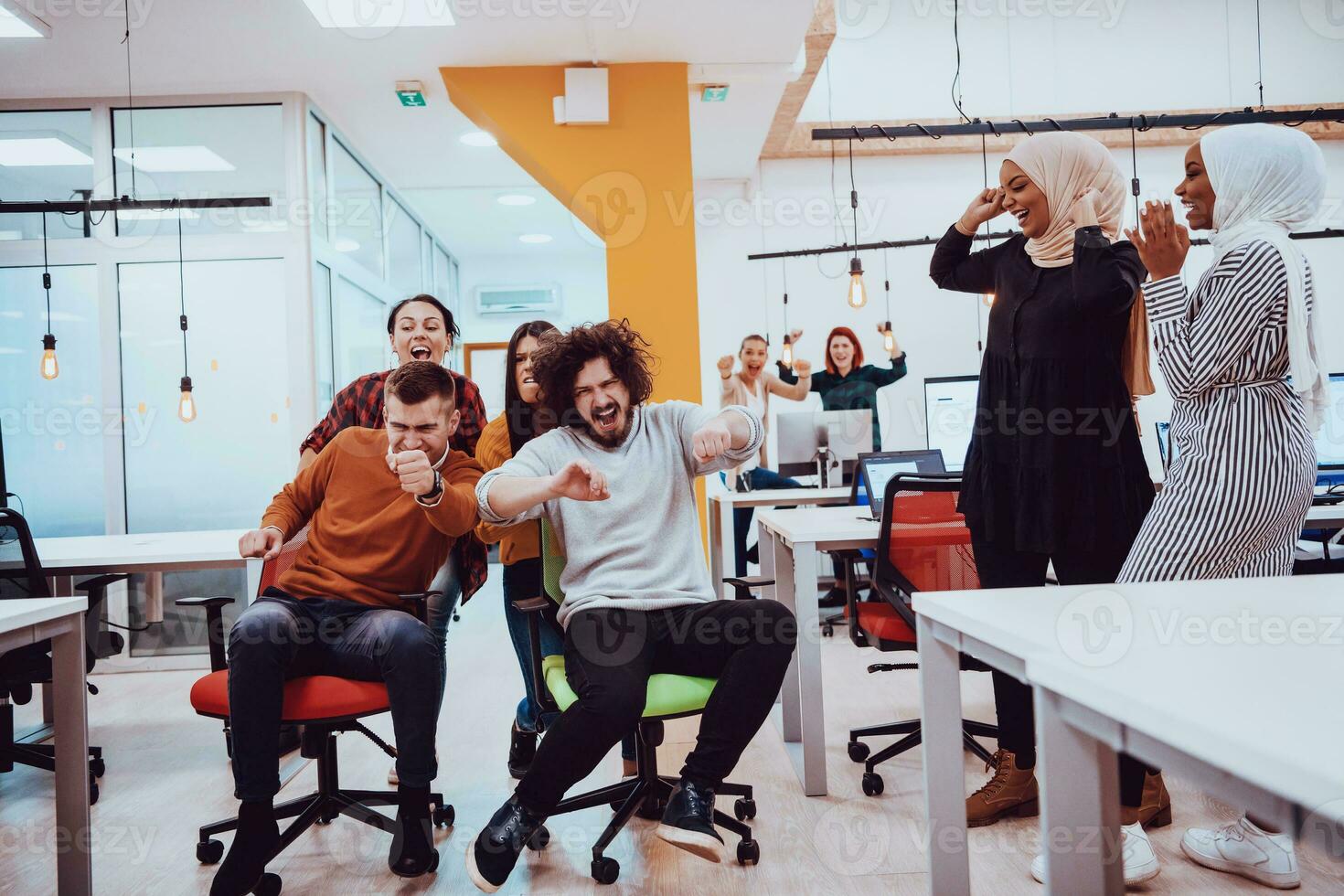 Team building and office fun. Young cheerful businesspeople in smart casual wear having fun while racing on office chairs and smiling. photo