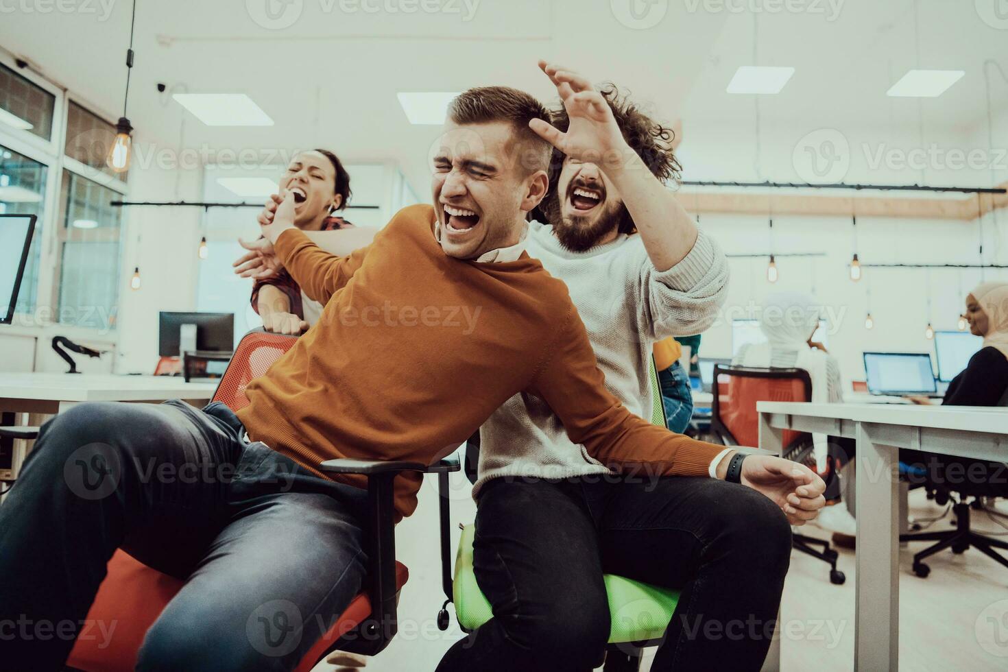 Team building and office fun. Young cheerful businesspeople in smart casual wear having fun while racing on office chairs and smiling. photo
