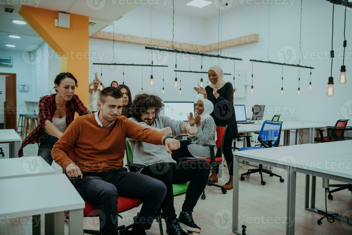 Team building and office fun. Young cheerful businesspeople in smart casual wear having fun while racing on office chairs and smiling. photo