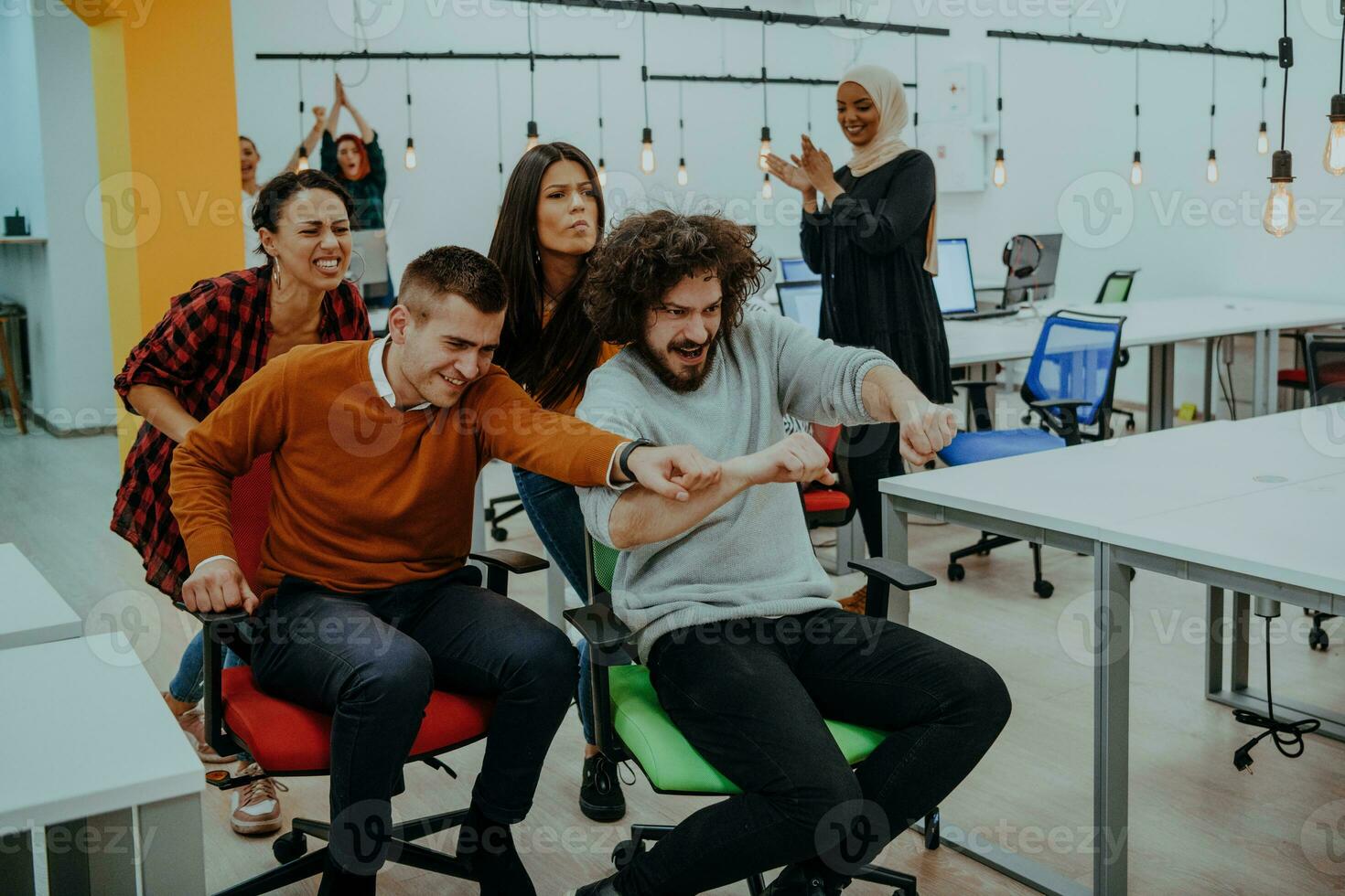 Team building and office fun. Young cheerful businesspeople in smart casual wear having fun while racing on office chairs and smiling. photo