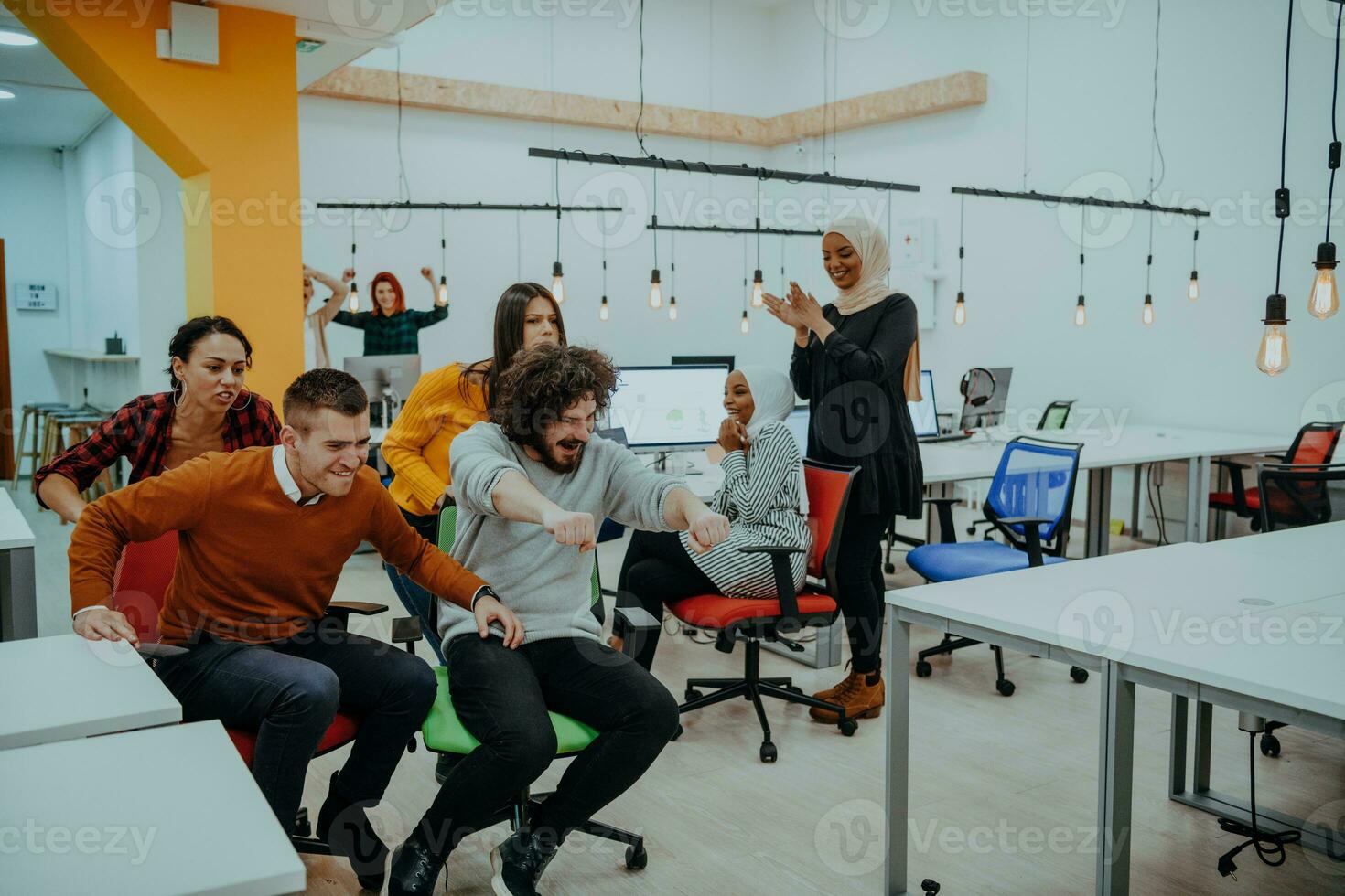 Team building and office fun. Young cheerful businesspeople in smart casual wear having fun while racing on office chairs and smiling. photo